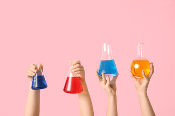 Female hands holding filled flasks on pink background. Chemistry lesson concept