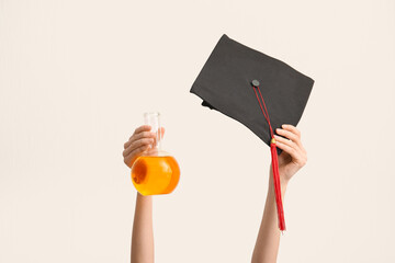 Female hands holding graduation hat with filled flask on white background. Chemistry lesson concept