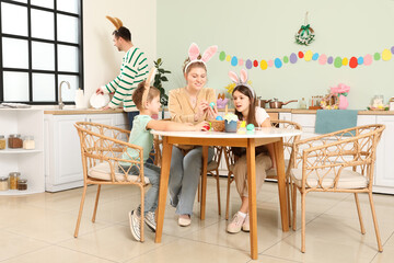 Mother with children painting festive Easter eggs in kitchen