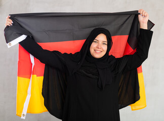 smiling Muslim woman in traditional black hijab holds flag of Germany. Portrait of female Muslim...