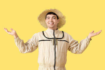 Male beekeeper in straw hat on yellow background