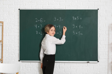 Cute boy writing on chalkboard during lesson in classroom