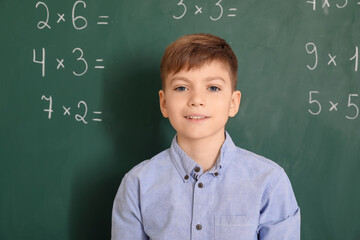 Cute boy near chalkboard during lesson in classroom
