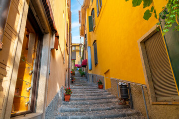 A narrow cobblestone alley with steps leading up the hill on a steep staircase with shops and cafes in the historic old town of Bellagio, Italy, on the shores of Lake Como.