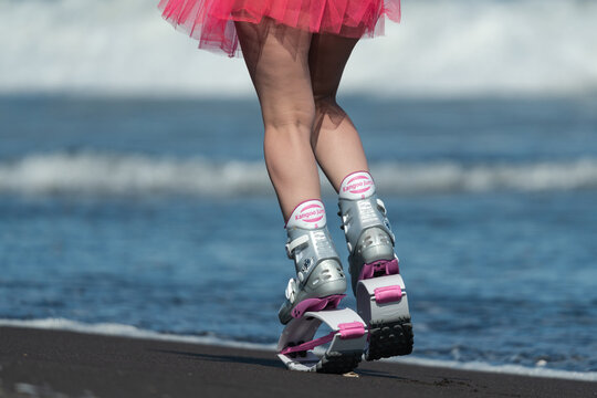 Rear cropped view of sportive woman legs in sports boots Kangoo Jumps and short pink skirt jumping and running on beach during aerobic training session outdoors. Kamchatka, Russia - June 15, 2022