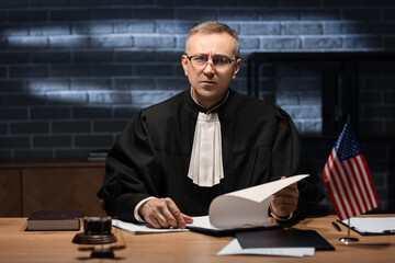 Mature judge with clipboard working at table in dark office