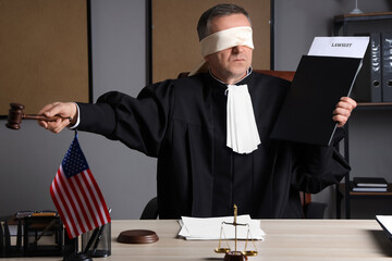 Blindfolded mature judge with lawsuit and gavel in dark office