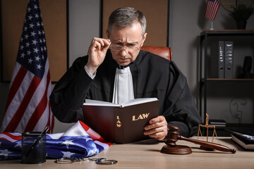 Mature judge reading law book at table in office