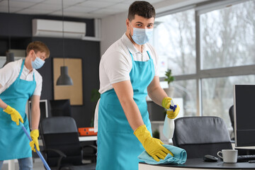 Male worker of cleaning service disinfecting table in office