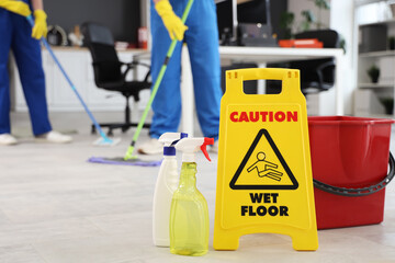 Caution sign with bottles of detergent and bucket on floor in office, closeup