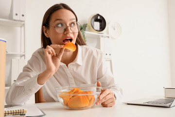 Young businesswoman eating potato chips at table in office