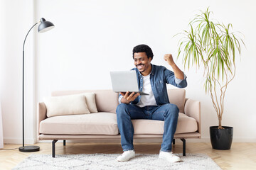 Black man excitedly using laptop at home