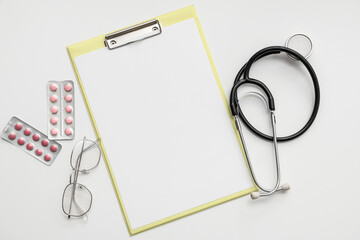 Blank clipboard with pills, stethoscope and eyeglasses on white background. World Health Day