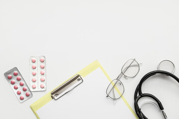 Blank clipboard with pills, stethoscope and eyeglasses on white background. World Health Day