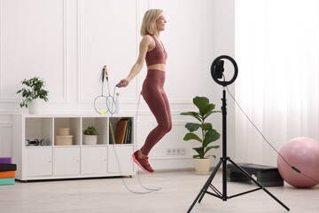 Smiling sports blogger jumping with rope while streaming online fitness lesson at home