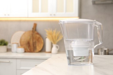 Water filter jug on white marble table in kitchen, space for text