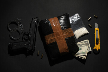 Drug packages with gun, handcuffs, money and utility knife on dark background