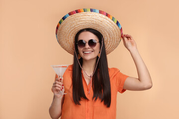 Young woman in Mexican sombrero hat with cocktail on beige background