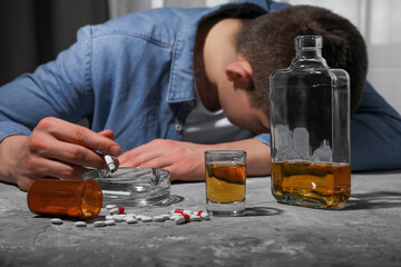 Alcohol and drug addiction. Man with smoldering cigarettes, whiskey and pills at grey textured...