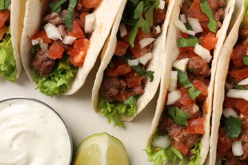Delicious meat tacos with vegetables, lime and sauce on light table, flat lay