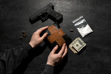 Man with drug package, gun and money on dark background