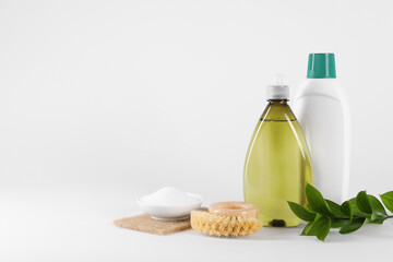 Bottles of cleaning product, brush, baking soda and green leaves on white background