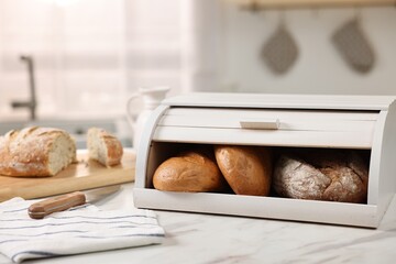 Wooden bread basket with freshly baked loaves and knife on white marble table in kitchen - obrazy, fototapety, plakaty