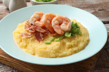 Plate with fresh tasty shrimps, bacon, grits and green onion on wooden table, closeup