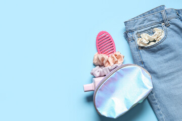 Jeans with trendy silk scrunchies, cosmetic bag and hairbrush on blue background