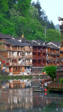Chinese tourist attraction destination - Feng Huang Ancient Town (Phoenix Ancient Town) on Tuo Jiang River with Wanming Pagoda tower and tourist boat. Hunan Province, China. Camera pan