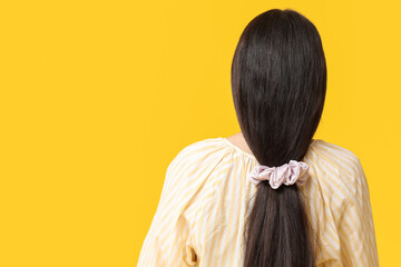 Woman with ponytail and silk scrunchy on yellow background, back view