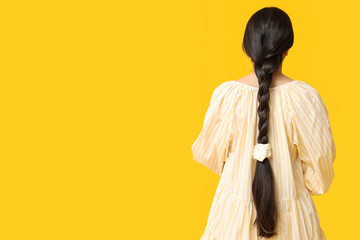 Woman with pigtail and silk scrunchy on yellow background, back view