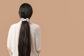 Woman with ponytail and silk scrunchy on beige background, back view