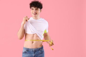 Handsome young happy sporty man with measuring tape on pink background. Weight loss concept