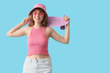 Beautiful young happy woman with skateboard on blue background - obrazy, fototapety, plakaty