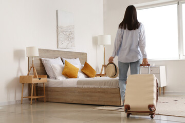 Woman with suitcase and hat in hotel room, back view