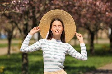 Beautiful young woman in park with blooming trees on sunny spring day