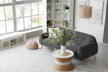 Vase with blooming branches on table in living room
