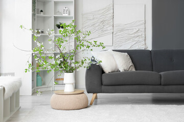 Stylish living room with cozy sofa and blooming branches