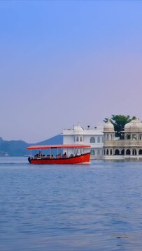 Famous luxury Udaipur Lake Palace Jag Niwas on island on lake Pichola on sunsets - Rajput architecture of Mewar dynasty rulers of Rajasthan. With tourist boat. Udaipur, India. Camera pan