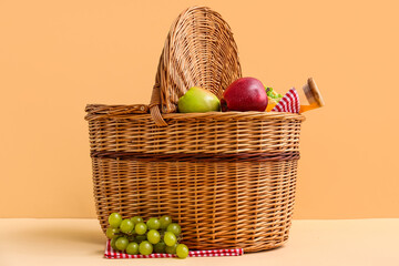 Wicker basket with tasty food and juice for picnic on table against beige background