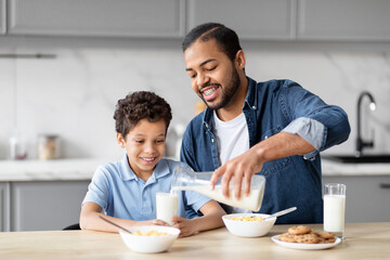 Obraz na płótnie Canvas Father pouring milk for son during breakfast