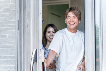 玄関で出迎える笑顔の若いアジア人夫婦
