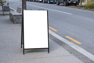 A blank white outdoor advertising stand or sandwich board mockup template. Background texture of a clear street signage board placed outdoors on a pedestrian sidewalk. Urban city environment.