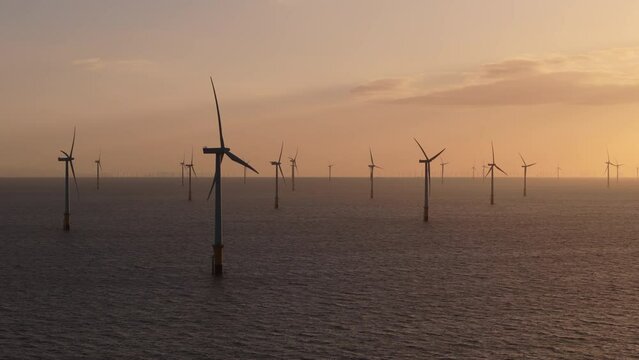 Beautiful view of offshore wind turbines spinning at sunset with dramatic sky and clouds in background