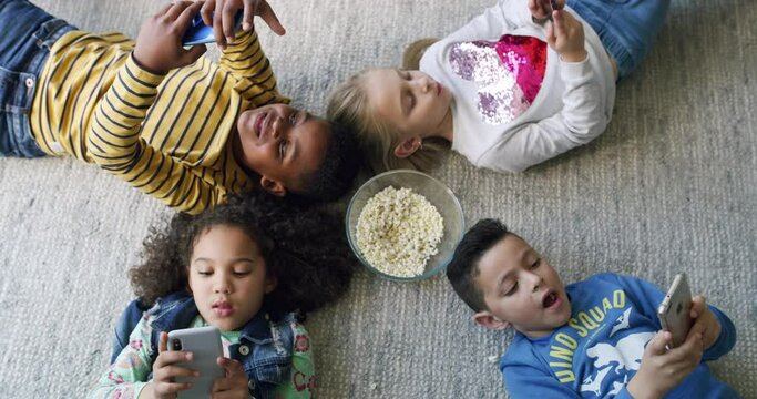 Phone, social media and popcorn with children on floor of living room in home together for browsing from above. Kids, internet and app with friends eating snack for bonding in apartment on weekend
