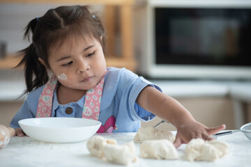 Little girl playing with bread dough placed on the table. she wanted to try making bread, preparing homemade bake - obrazy, fototapety, plakaty