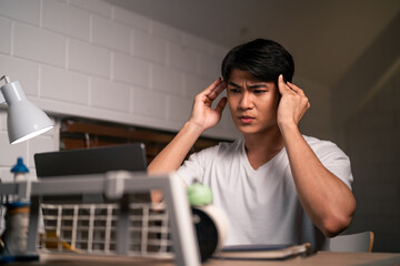Asian depressed young man overworking alone on working table at night.