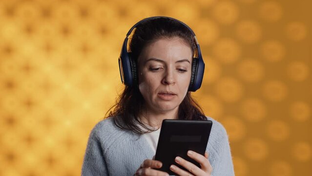 Woman wearing headphones, practicing new language using internet app on digital tablet, isolated over studio background. Person repeating foreign words, reading them on device