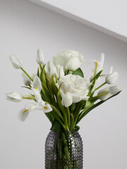 White flowers in a transparent ribbed vase, against a white wall background